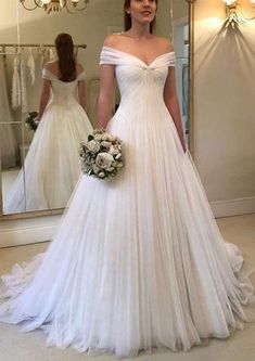 a woman standing in front of a mirror wearing a wedding dress with pleated skirt