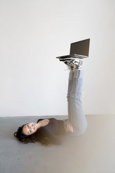 a woman laying on the ground with her laptop in her hand and holding it above her head