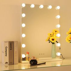 a table with a mirror and flowers on it next to a box of makeup brushes