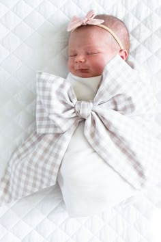 a baby wrapped in a bow laying on top of a white blanket with it's eyes closed