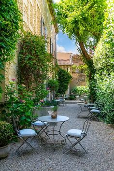 an outdoor patio with tables and chairs surrounded by greenery in the middle of a courtyard