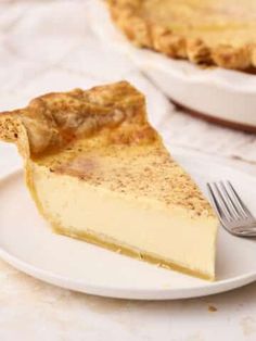 a piece of pie on a white plate with a fork next to it and another pie in the background