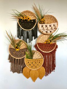 four woven baskets with flowers and grass hanging on the wall in front of a white wall