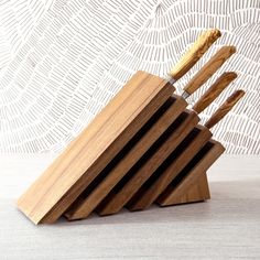 a wooden block with six knives in it on a table next to a white wall