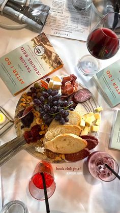 a platter of cheese, crackers and grapes on a table with wine glasses