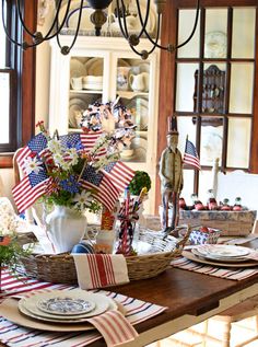 a dining room table set with american flags and flowers in a basket on top of it