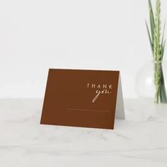 a thank card with the words, thank you in gold foil on it next to a green plant