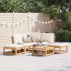 an outdoor patio with wooden furniture and string lights strung over the privacy wall behind it