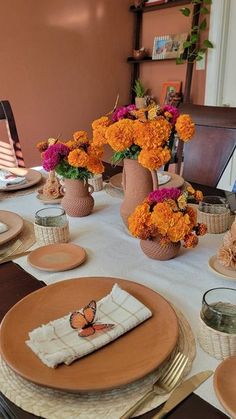 the table is set with plates, napkins and vases filled with orange flowers