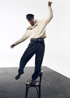 a man sitting on top of a chair with his arms in the air while wearing a hat