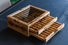 an open wooden box with drawers sitting on top of a blue tableclothed surface