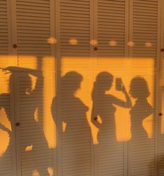 the shadow of three people standing in front of a wall with shutters on it