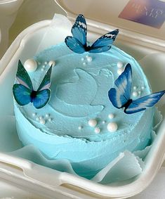 two blue butterflies on top of a frosted cake in a plastic container with pearls