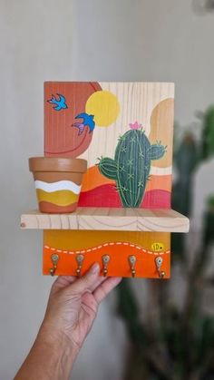 a hand holding up a wooden shelf with cactus paintings on it