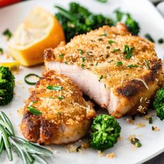 two pieces of meat and broccoli on a white plate with lemon wedges