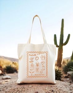 a white tote bag sitting on top of a rock next to a cacti