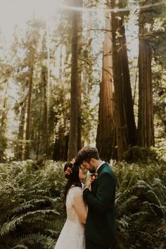 a bride and groom standing in the middle of a forest surrounded by tall redwood trees