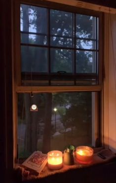 two candles are sitting on a window sill in front of a book and some books