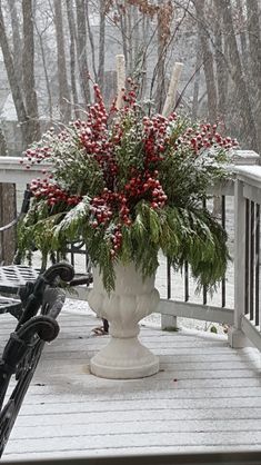 a white vase filled with red berries sitting on top of a wooden deck next to a bike