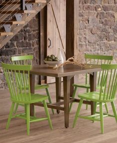 a wooden table with four green chairs next to a stair case in a stone walled room