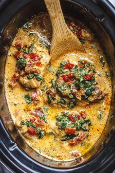 a wooden spoon in a crock pot filled with chicken, spinach and tomatoes