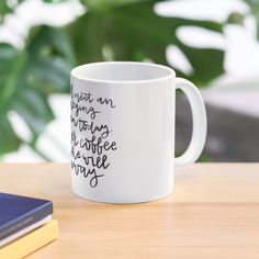 a white coffee mug sitting on top of a wooden table next to a book and plant