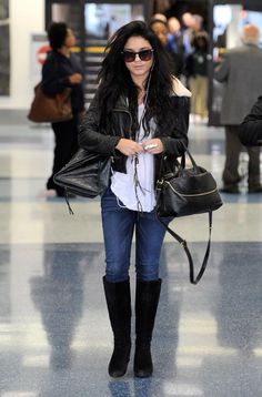 a woman walking through an airport carrying a black handbag and wearing knee high boots