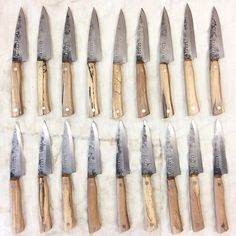 many knives are lined up in rows on a white tablecloth with wood and metal handles