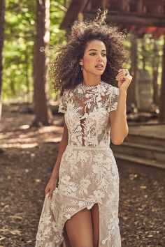 a woman in a white dress is walking through the woods with her hand on her hip