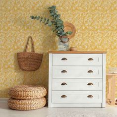 a white dresser sitting next to a yellow wall with a basket on top of it