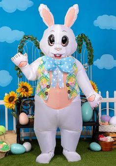 an inflatable easter bunny is standing on the grass with eggs and flowers around it