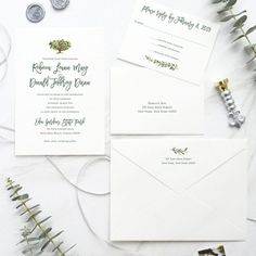 the wedding stationery is laid out on a white table with greenery and coins