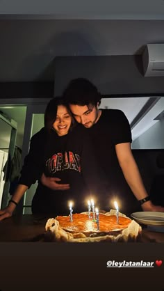 a man and woman standing in front of a cake with lit candles on it that says happy birthday