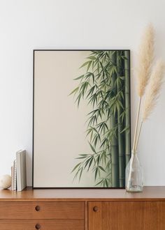 a bamboo plant in a glass vase on top of a wooden dresser next to a white wall