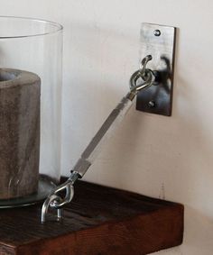 a candle is chained to a wall with a glass holder on the side and a metal chain attached to it