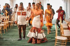 a man and woman walking down the aisle at a wedding ceremony with other people behind them