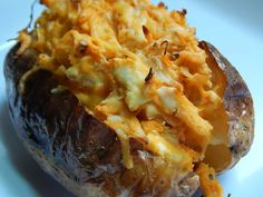 a baked potato with cheese on it sitting on a white plate in front of the camera