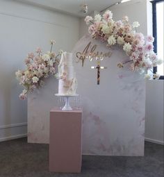 a table topped with a cake next to a wall covered in pink and white flowers