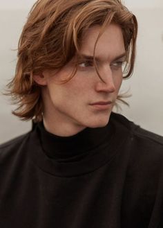 a young man with long hair wearing a black turtle neck shirt and looking off to the side