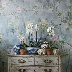 an old dresser with flowers and vases on it in front of a floral wallpaper