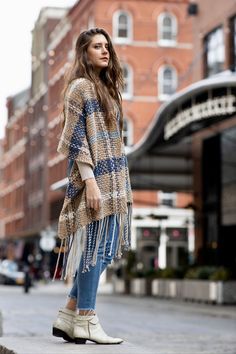 a woman is standing on the sidewalk wearing boots and a plaid coat with fringes