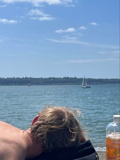 a man sitting on the beach with his head down looking out at the water and sailboats in the distance