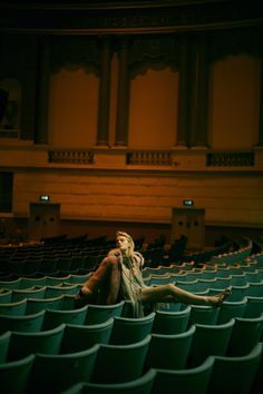 a woman sitting in the middle of an empty auditorium with her legs up on the floor