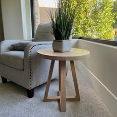 a small table with a potted plant on it next to a chair and window