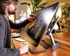 a man is drawing on a large screen monitor with a pen in his hand while sitting at a desk