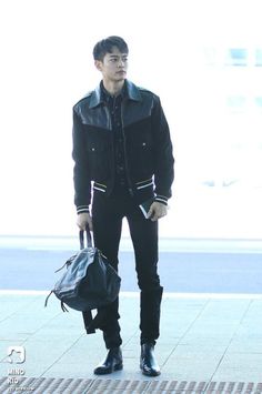 a young man is standing on the sidewalk with his hand in his pocket and holding a black bag