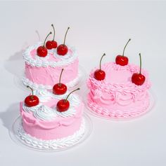 two pink cakes with cherries on top and one has a cherry on the top