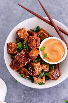 a white bowl filled with tofu and chopsticks on top of a table