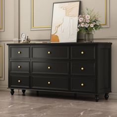 a black dresser with flowers on top and a framed photograph above it's drawers