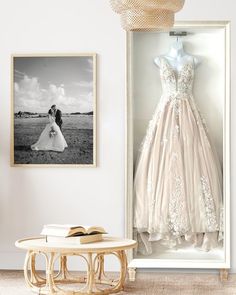 a wedding dress hanging on the wall next to a table with an open book in front of it